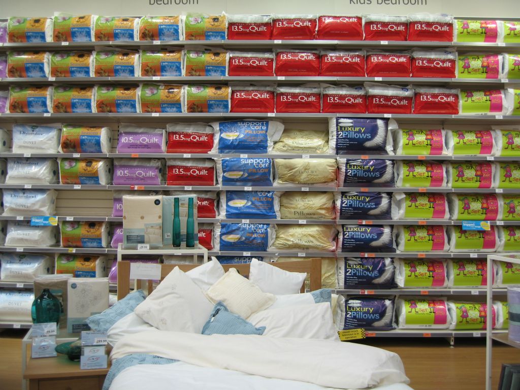 A wall counter loaded with continental quilts and pillows, apparently at random with no logic to the display sequence