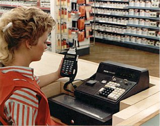 A colleague uses a Telxon PTC-701 Hand-held terminal to extract departmental sales and items sold data from an Anker Data Systems ADS till in a Woolworths store in 1987.