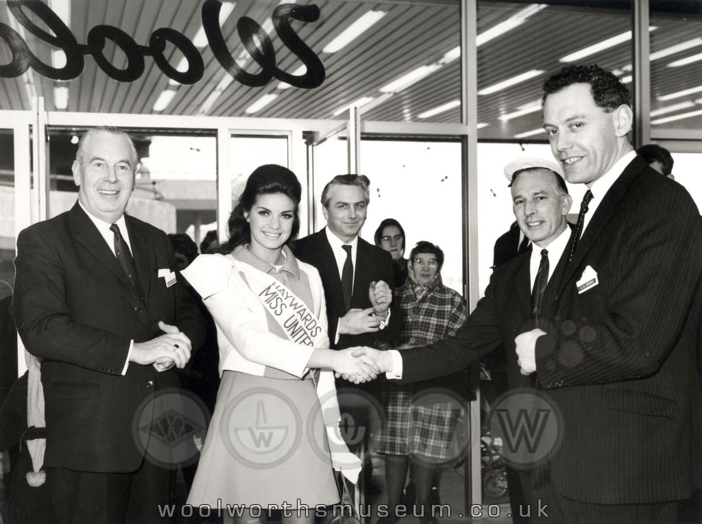 Woolco's Commissionaire shakes hands with Kathleen Winstanley on her arrival at the Teeside store, as Buying Manager Sid (A.S.) Stafford (left) and General Manager John G. Dodds look on