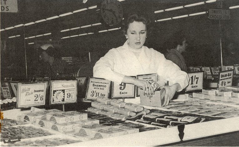 A staff member tidies the toiletries display on a personal service counter at the front of a Woolworth store in the 1950s